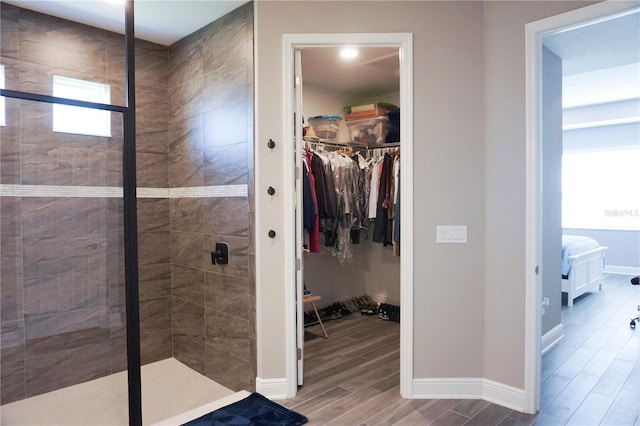 full bathroom featuring wood finish floors, a walk in closet, baseboards, and a stall shower