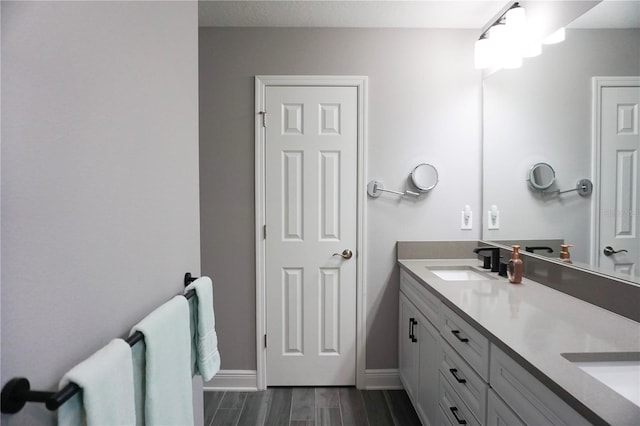 full bath featuring double vanity, wood finished floors, baseboards, and a sink