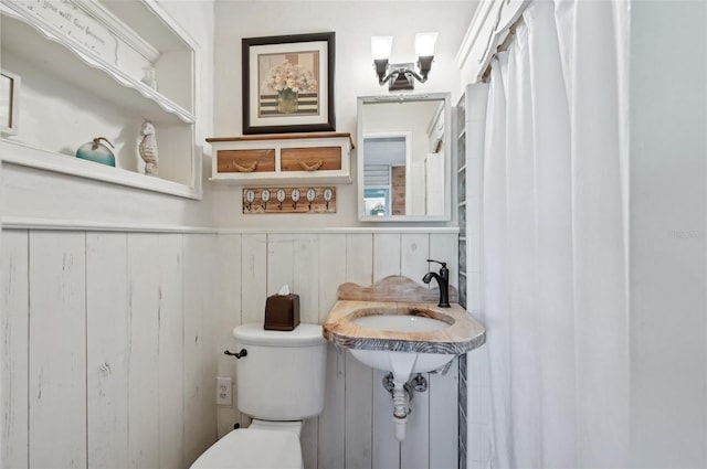 bathroom with a wainscoted wall, wood walls, a sink, and toilet