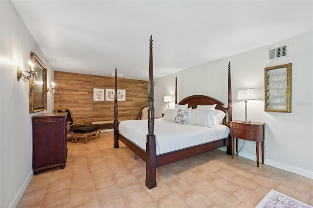 bedroom with an accent wall, visible vents, wooden walls, and baseboards