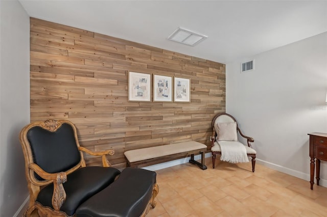 sitting room featuring wood walls, baseboards, an accent wall, and visible vents