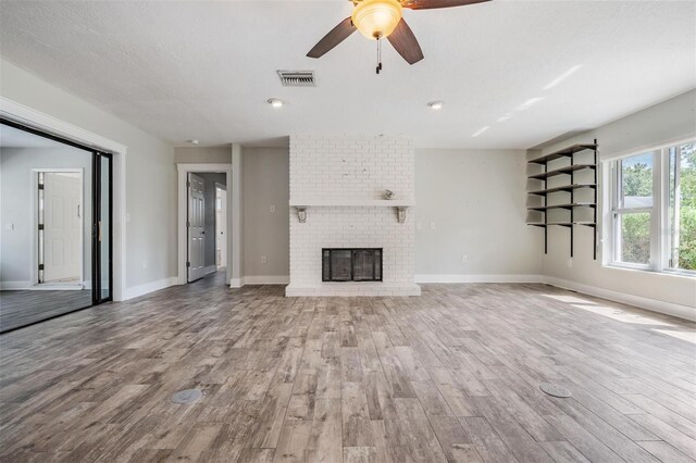 unfurnished living room with brick wall, ceiling fan, a brick fireplace, and hardwood / wood-style flooring