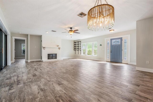 unfurnished living room featuring a fireplace, hardwood / wood-style floors, ceiling fan with notable chandelier, a textured ceiling, and brick wall