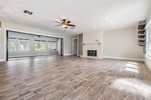 unfurnished living room with brick wall, ceiling fan, light hardwood / wood-style floors, and a brick fireplace