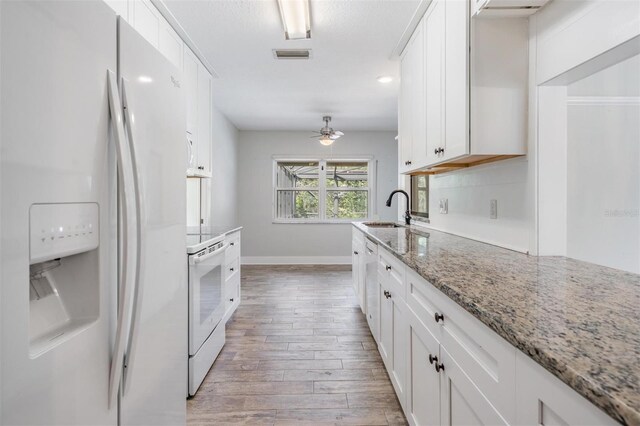 kitchen with light wood-type flooring, white appliances, light stone counters, white cabinetry, and ceiling fan