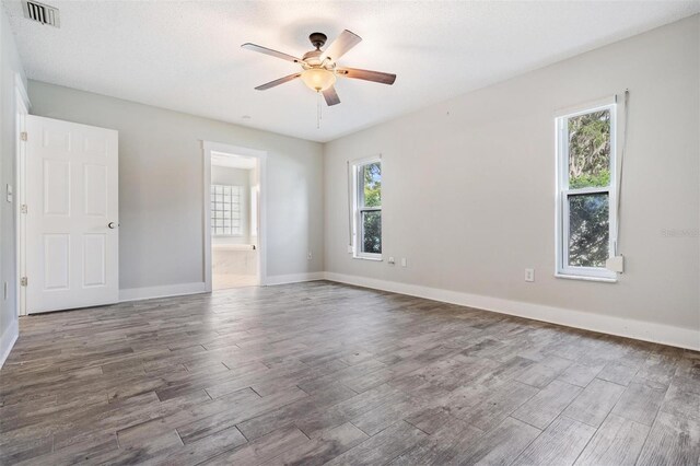 unfurnished bedroom with ensuite bath, multiple windows, wood-type flooring, and ceiling fan