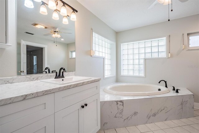 bathroom with tiled tub, ceiling fan, vanity, and a healthy amount of sunlight