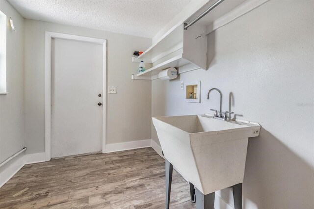 laundry room featuring sink, hookup for a washing machine, light hardwood / wood-style floors, and a textured ceiling