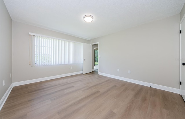 empty room with light wood-type flooring and a textured ceiling