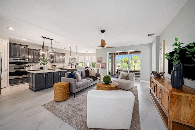 living room featuring ceiling fan with notable chandelier and a textured ceiling