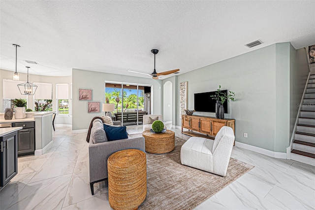 living room with ceiling fan with notable chandelier and a textured ceiling