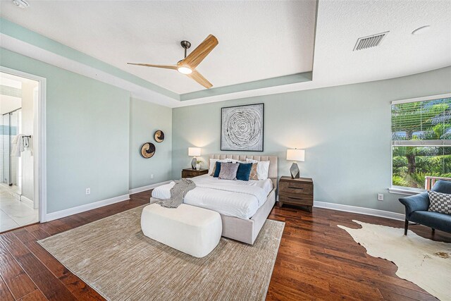 bedroom featuring a textured ceiling, ceiling fan, dark hardwood / wood-style floors, a raised ceiling, and ensuite bathroom