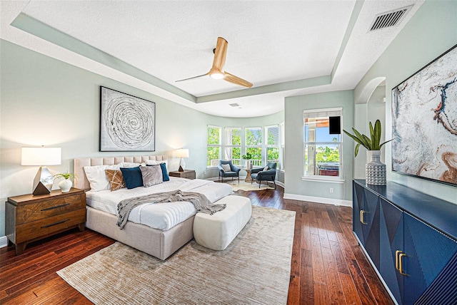 bedroom featuring a textured ceiling, dark wood-type flooring, ceiling fan, and a tray ceiling