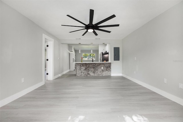 unfurnished living room with ceiling fan, electric panel, and light hardwood / wood-style flooring