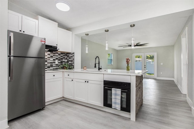 kitchen featuring light wood-type flooring, stainless steel fridge, tasteful backsplash, kitchen peninsula, and sink