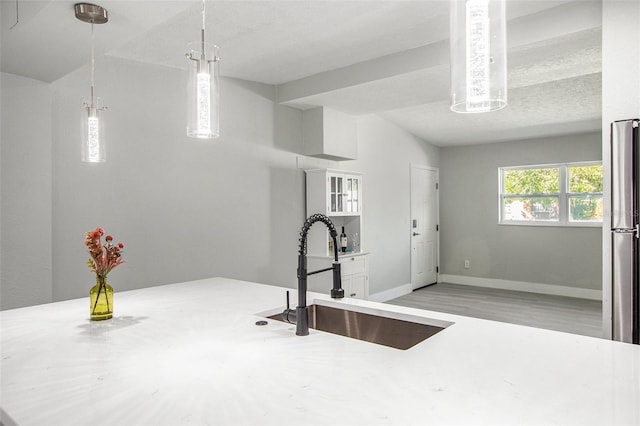 kitchen featuring white cabinets, light wood-type flooring, decorative light fixtures, sink, and a textured ceiling