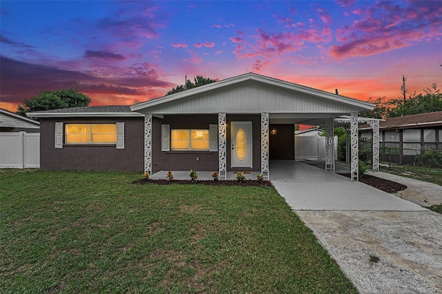 view of front of house with an attached carport, brick siding, fence, a yard, and concrete driveway