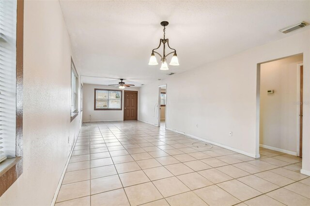 tiled spare room with ceiling fan with notable chandelier