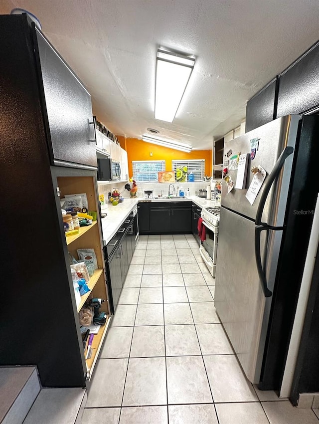 kitchen featuring a textured ceiling, light tile patterned floors, vaulted ceiling, sink, and appliances with stainless steel finishes