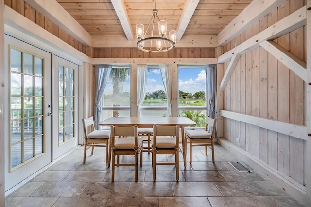 unfurnished dining area featuring wooden ceiling, beam ceiling, a notable chandelier, wooden walls, and french doors