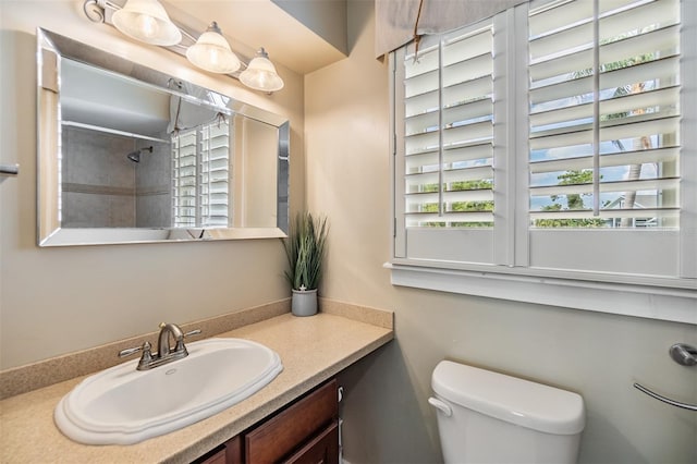 bathroom featuring a tile shower, vanity, and toilet