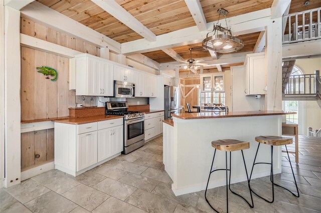 2118 Harbour Watch Dr, Tarpon Springs, FL 34689 - kitchen with appliances with stainless steel finishes, wood walls, a ceiling fan, white cabinetry, and wooden ceiling with exposed beams