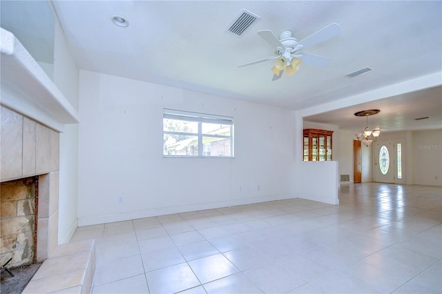 unfurnished living room featuring ceiling fan with notable chandelier, a tiled fireplace, and light tile patterned flooring