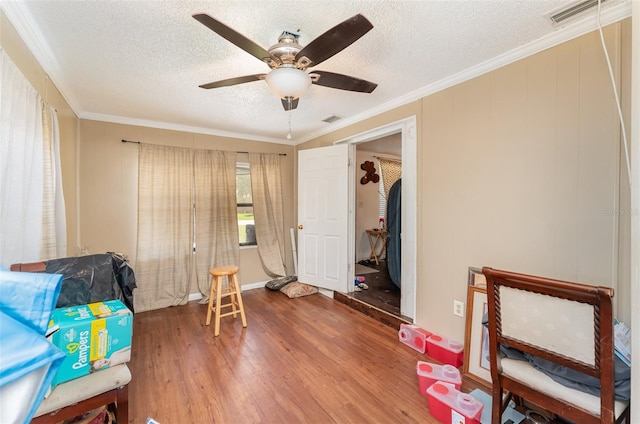 living area featuring wood-type flooring, a textured ceiling, crown molding, and ceiling fan