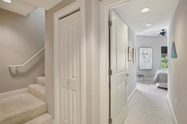 hallway featuring stairs, baseboards, and light colored carpet