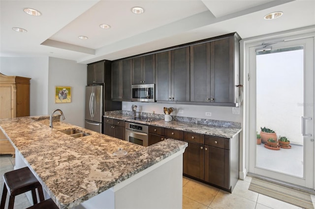 kitchen with light stone counters, a kitchen island with sink, stainless steel appliances, a kitchen bar, and a sink