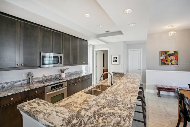 kitchen with light tile patterned floors, stainless steel appliances, a sink, light stone countertops, and an island with sink