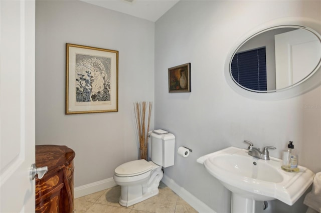 half bath with toilet, baseboards, a sink, and tile patterned floors