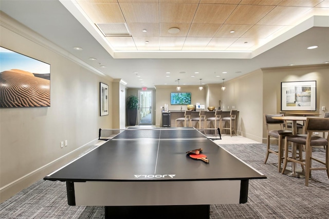 recreation room with ornamental molding, carpet flooring, a raised ceiling, and a community bar