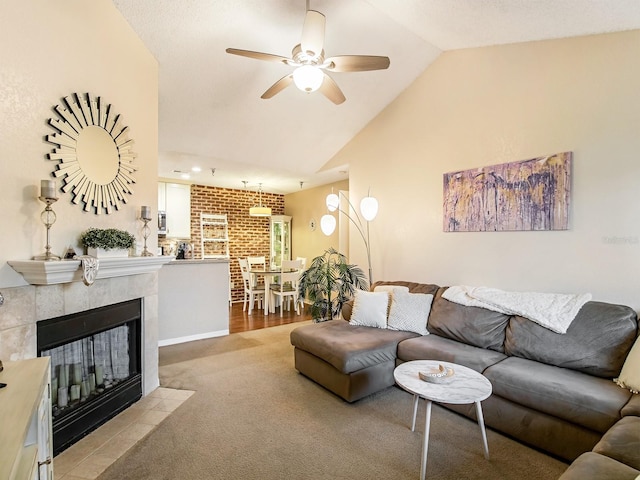 living room with light wood-type flooring, ceiling fan, a tiled fireplace, and vaulted ceiling