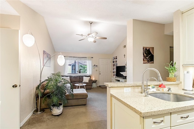 kitchen featuring cream cabinetry, sink, ceiling fan, light stone countertops, and vaulted ceiling