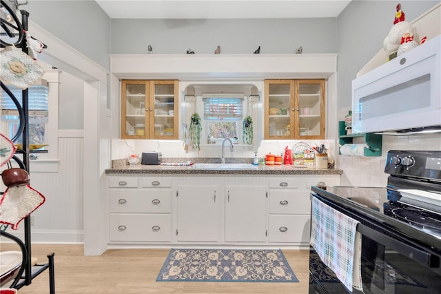 kitchen with white cabinets, light stone countertops, black / electric stove, light hardwood / wood-style floors, and sink