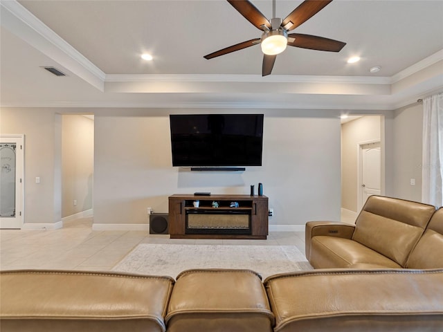 living room featuring tile patterned flooring, a fireplace, crown molding, a tray ceiling, and ceiling fan