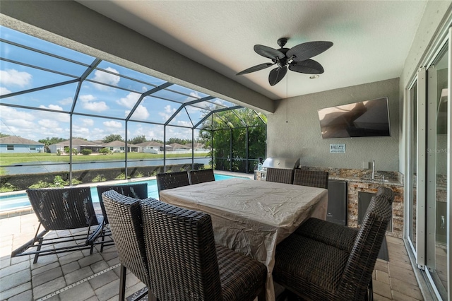 view of patio featuring a grill, glass enclosure, sink, a water view, and ceiling fan