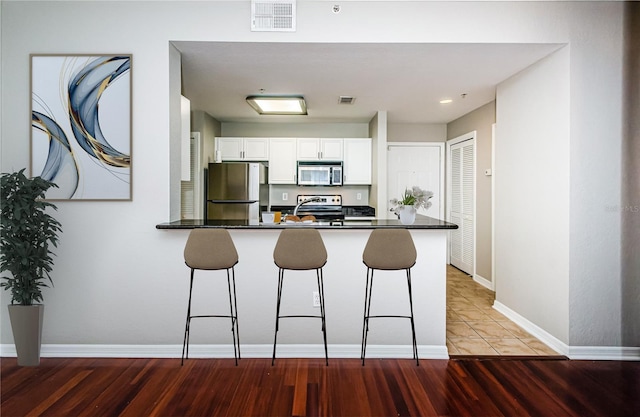 kitchen featuring tile patterned flooring, a breakfast bar area, stainless steel appliances, kitchen peninsula, and white cabinetry