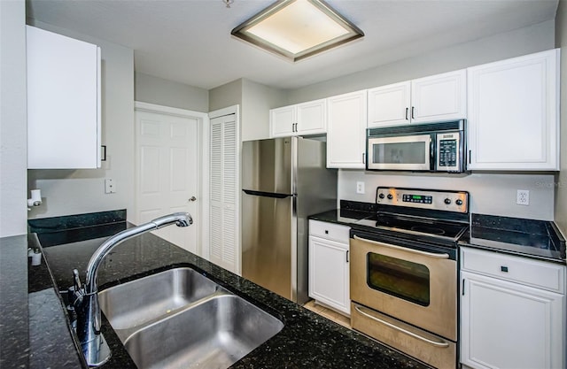 kitchen featuring stainless steel appliances, white cabinets, sink, and dark stone counters