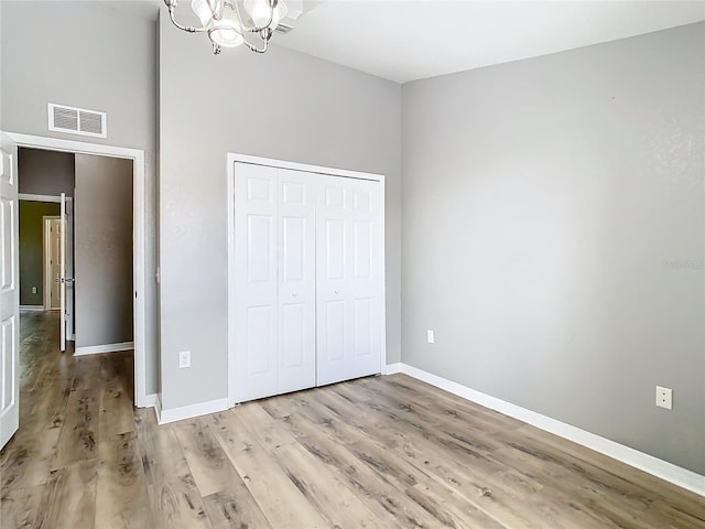 unfurnished bedroom featuring a chandelier, a towering ceiling, light hardwood / wood-style flooring, and a closet