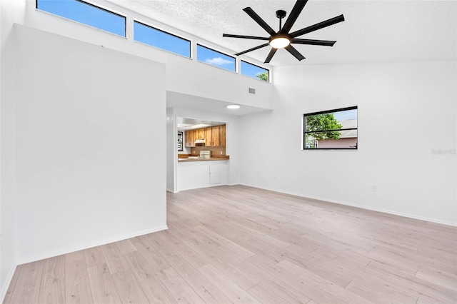 unfurnished living room with high vaulted ceiling, light hardwood / wood-style floors, a textured ceiling, and ceiling fan