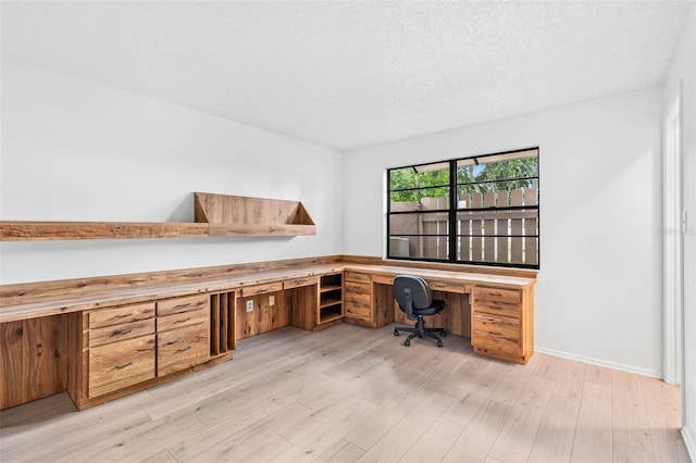 unfurnished office with light wood-type flooring, built in desk, and a textured ceiling