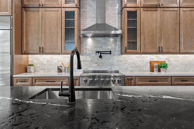 kitchen featuring stove, backsplash, stainless steel built in fridge, and wall chimney range hood