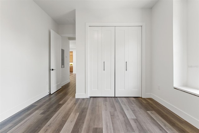 unfurnished bedroom with a closet, wood finished floors, and baseboards