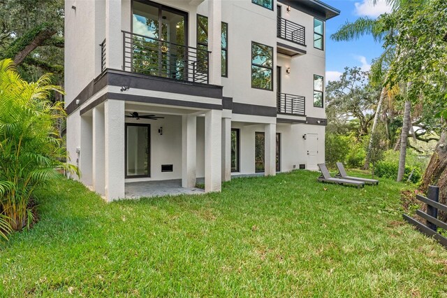 rear view of property featuring ceiling fan, a patio area, a balcony, and a yard