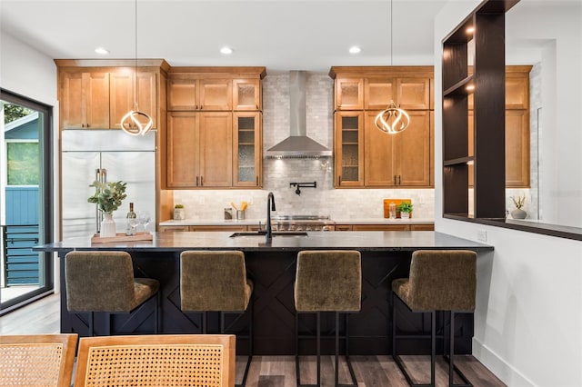 kitchen with wood finished floors, a sink, backsplash, wall chimney exhaust hood, and a kitchen bar