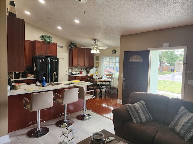 kitchen featuring black fridge with ice dispenser, tasteful backsplash, light hardwood / wood-style flooring, ceiling fan, and lofted ceiling