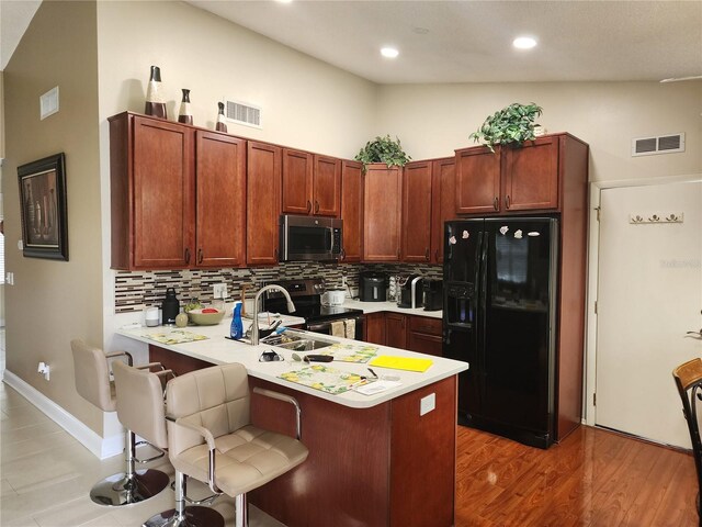 kitchen with stainless steel appliances, light hardwood / wood-style floors, a breakfast bar area, kitchen peninsula, and high vaulted ceiling