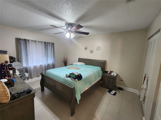 bedroom featuring a textured ceiling, light tile patterned floors, ceiling fan, and a closet